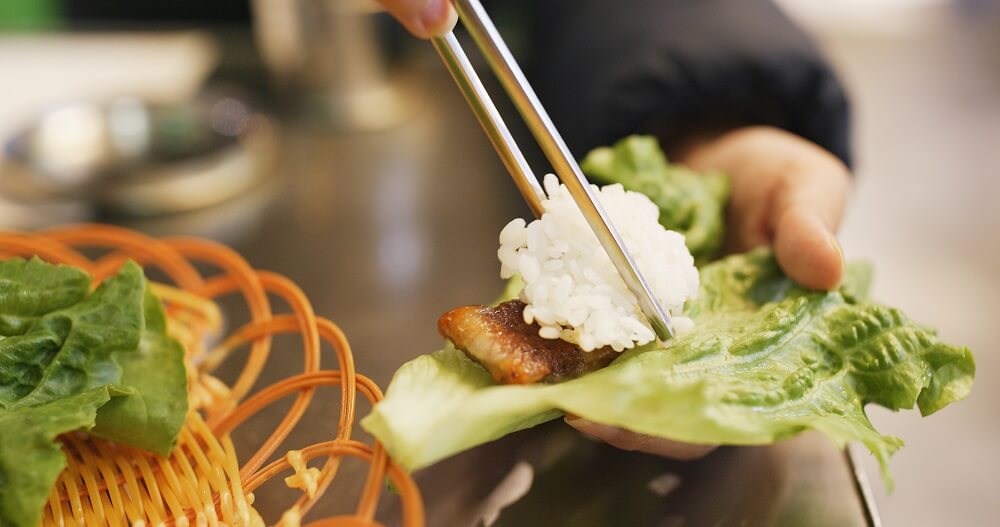 Woman wrapping grilled korean meat in lettuce at restaurant